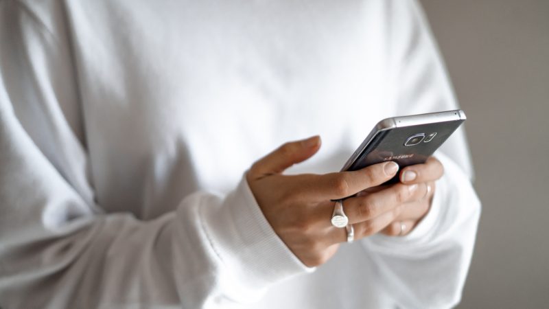 person in white jumper texting on a phone