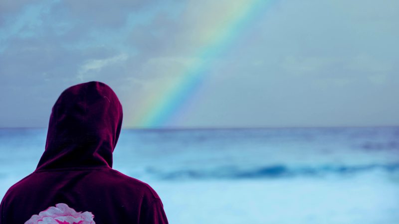Person in hoodie watching rainbow over the sea