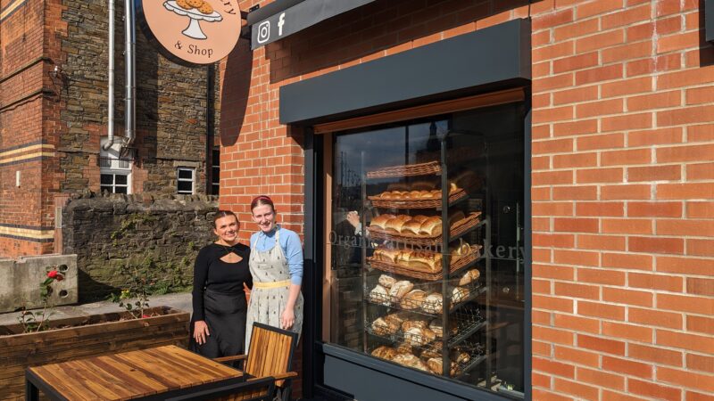 Rosa and Coastal employee outside Rosa's bakery with a window of bread and table and chairs