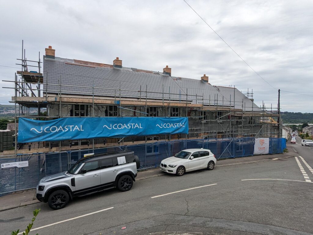 Street view photo of part built rows of houses with scaffolding with Coastal banner